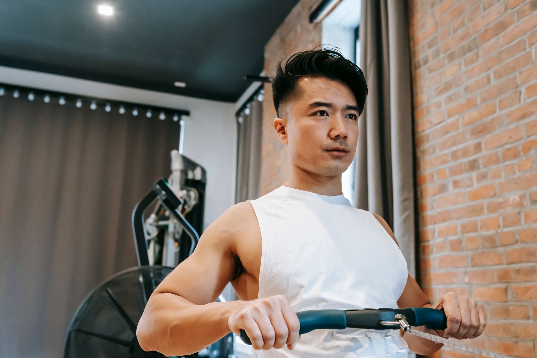Young ethnic strong male with trendy hairstyle training on rowing machine in sport club