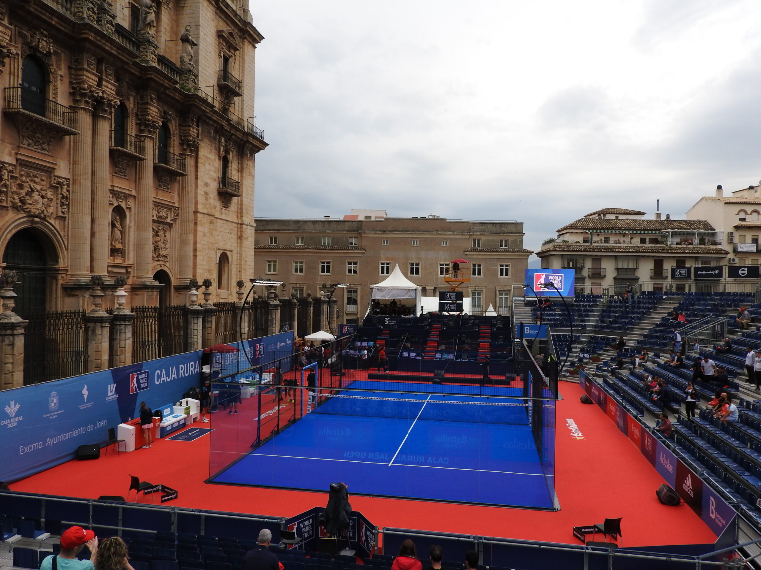 Lapangan padel biru di alun-alun Katedral Jaén, Spanyol, lengkap dengan tribun penonton dan panel sponsor turnamen World Padel Tour.
