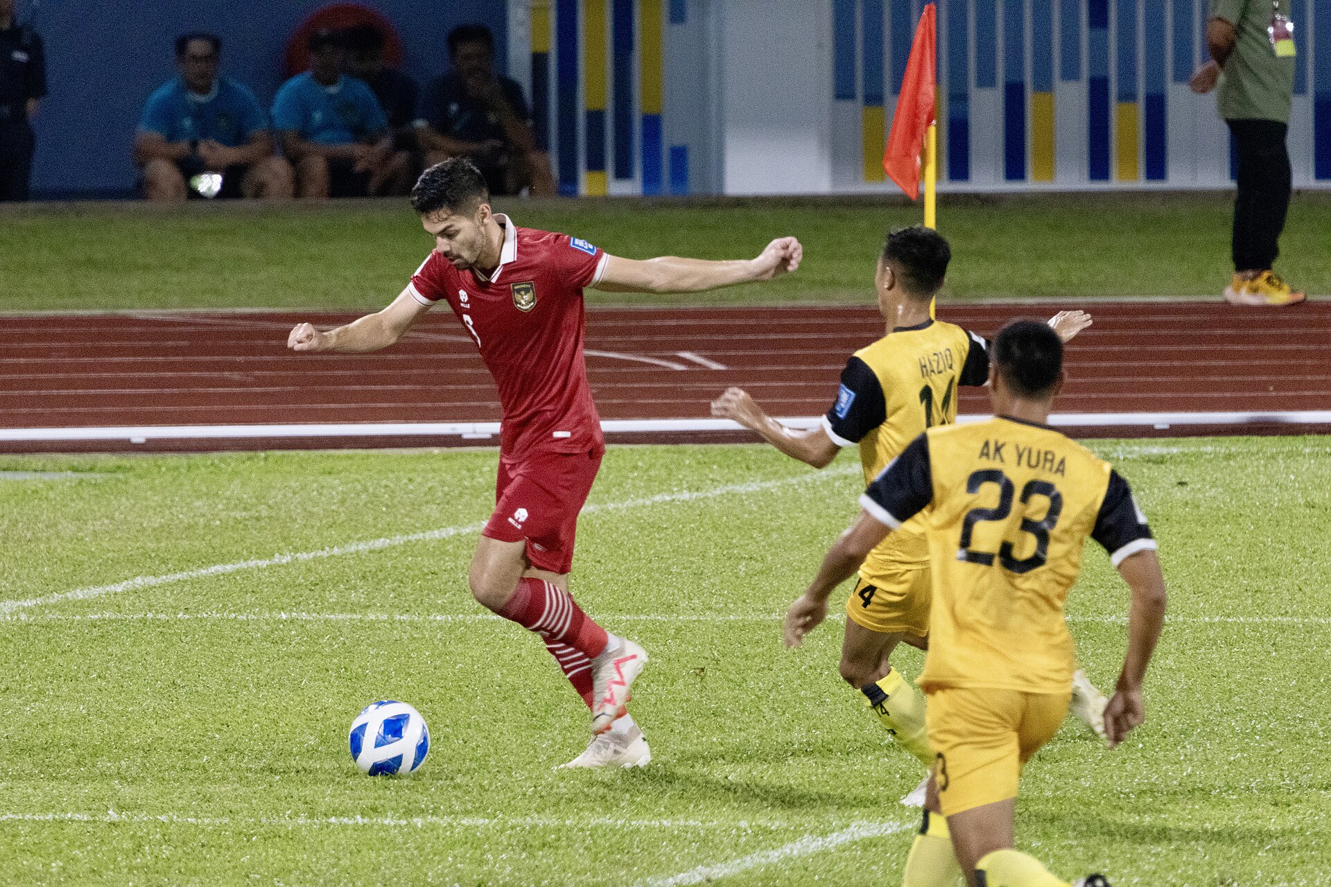 Pemain Timnas Indonesia berseragam merah menggiring bola dekat bendera sepak pojok sambil dibayangi dua pemain lawan berseragam kuning