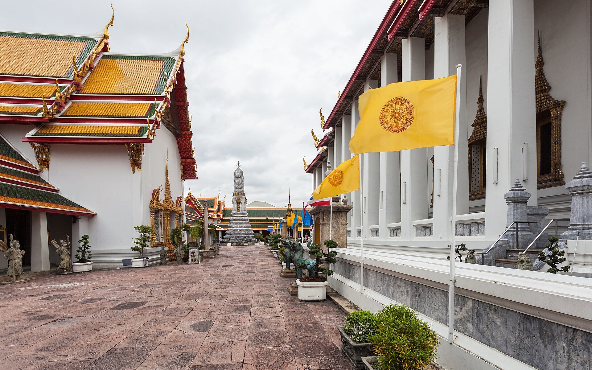 Halaman kompleks kuil Wat Pho di Bangkok dengan atap bertingkat berwarna oranye-hijau dan bendera kuning