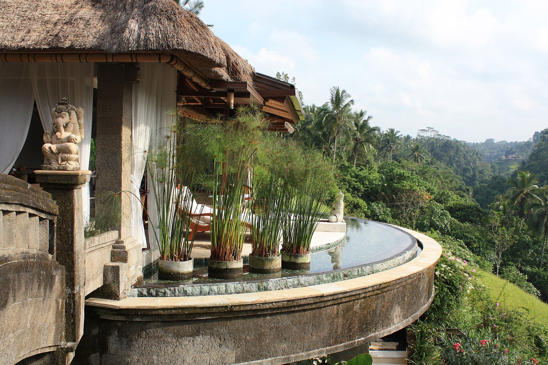 Paviliun beratap alang-alang dan kolam tanpa tepi melengkung yang menghadap lembah hutan tropis di Ubud, Bali