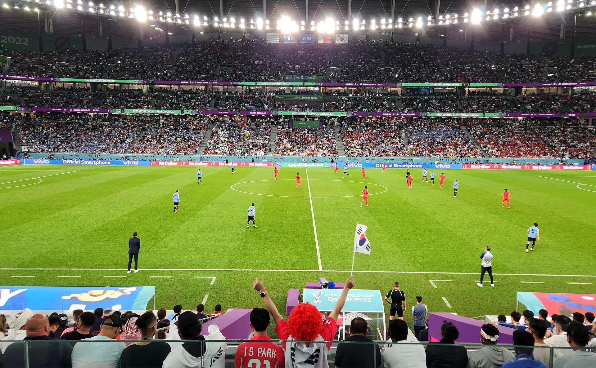 Laga Piala Dunia 2022 antara Korea Selatan dan Uruguay di Education City Stadium, Doha, dilihat dari tribun, dengan seorang suporter berwig merah mengibarkan bendera Korea Selatan di barisan depan.